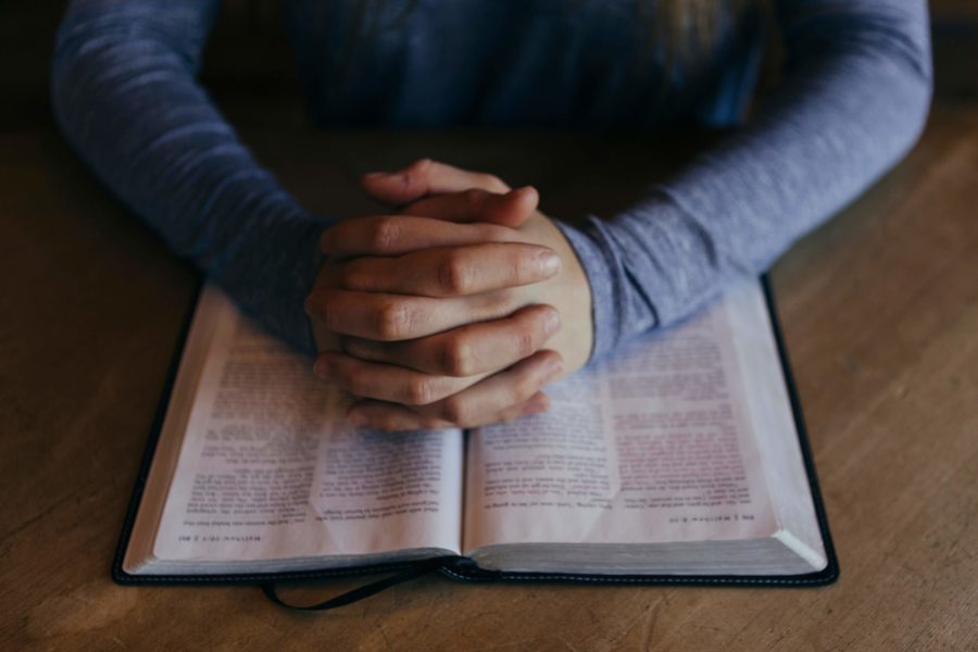 hands clasped in prayer over an open book
