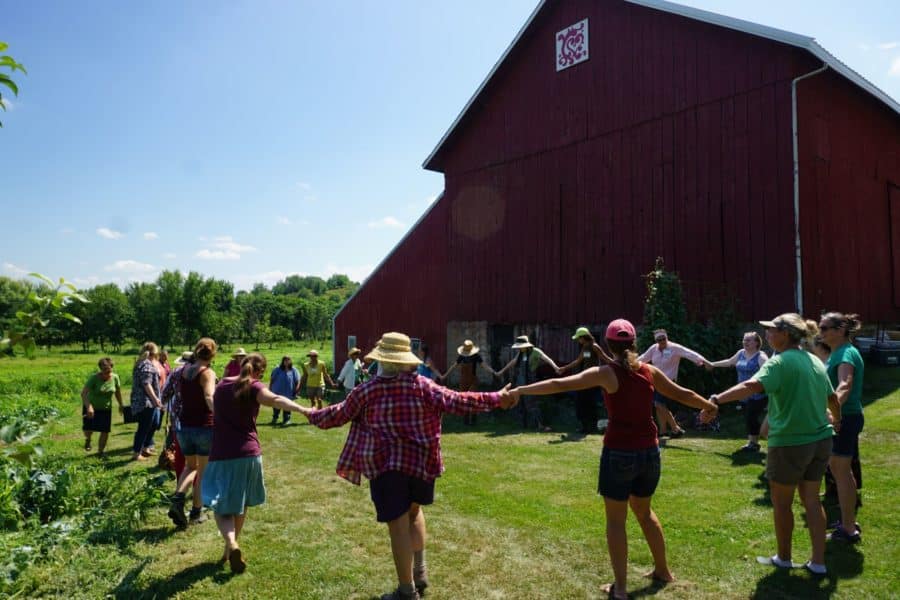Women stand around in a circle holding hands at the annual Soil Sisters gather of women farmers.