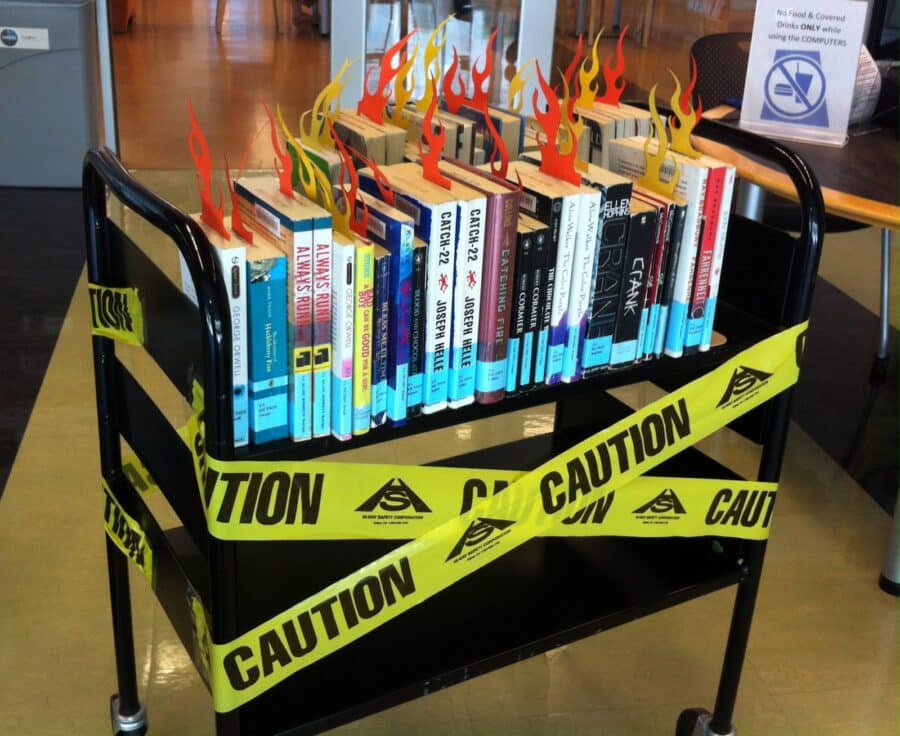 Library books sit on a shelf crossed with caution tape and flame-shaped bookmarks.