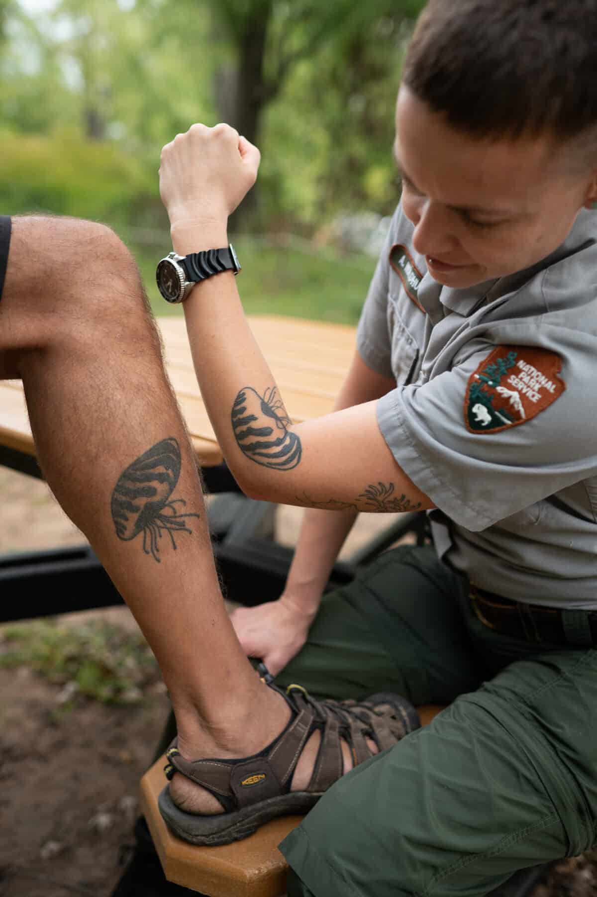 Byron Karns, 63, of Ely, MN, and Allie Holdhusen, 37, of Minneapolis, MN, show off their tattoos of zebra mussels on September 11, 2023 in Taylors Falls, MN. The original drawings were done by Holdhusen.